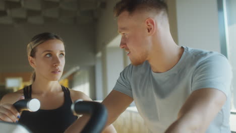 man cycling in gym with help of female instructor