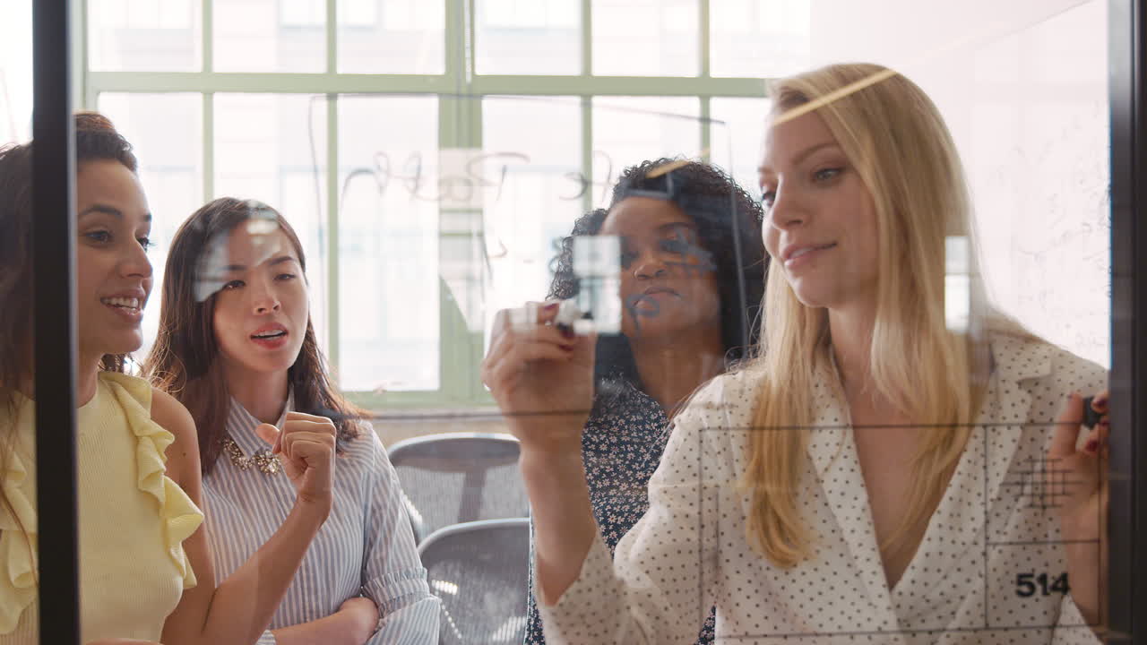 네 명의 여성 크리에이티브가 유리 벽에 아이디어를 모으고 있습니다.