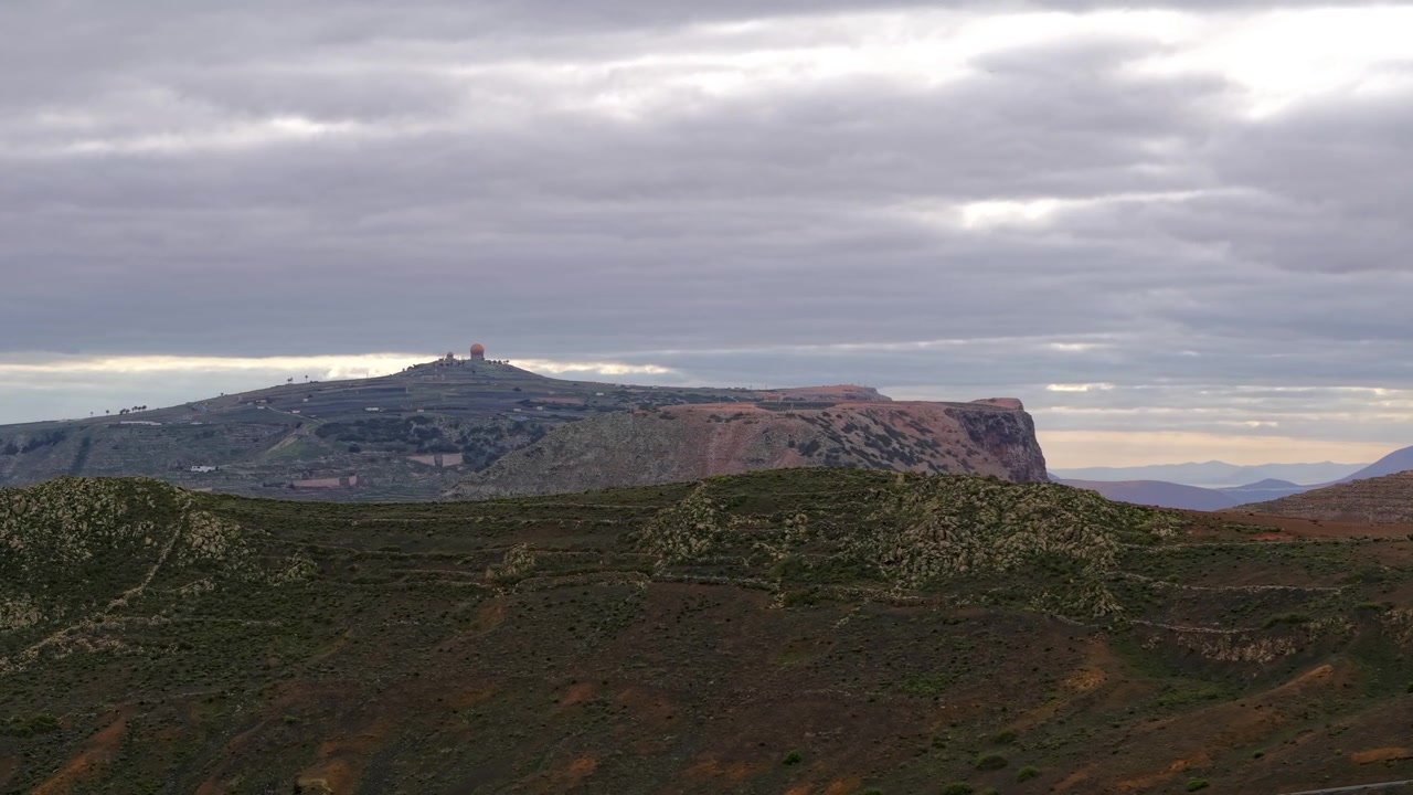 Paesaggio vulcanico aspro e montagna distante con stazione radar militare di Pézenas del Chache, Lanzarote, Spagna. Vista panoramica aerea con drone, spazio per il testo.