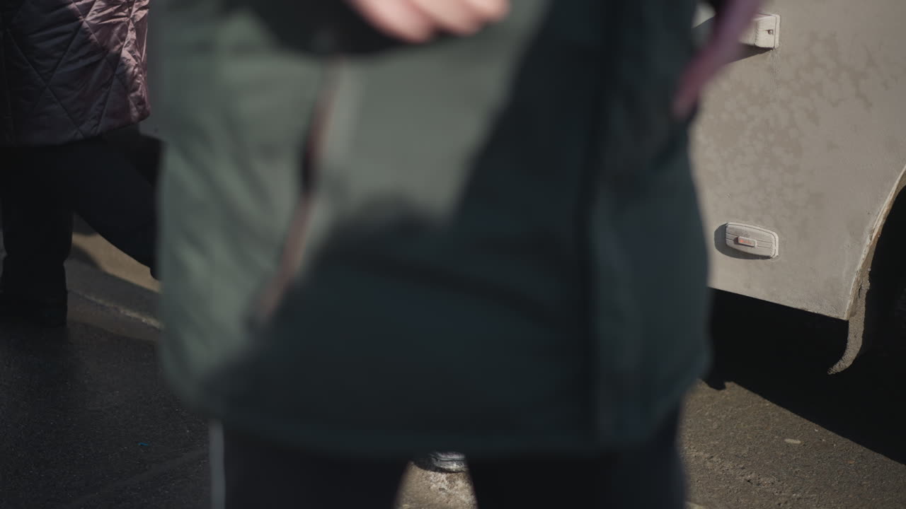 lower view shows passenger waiting beside bus door as riders step down, then boarding via steps, shadow over curb and asphalt, winter sun on street, transit pause before doors close and bus departs