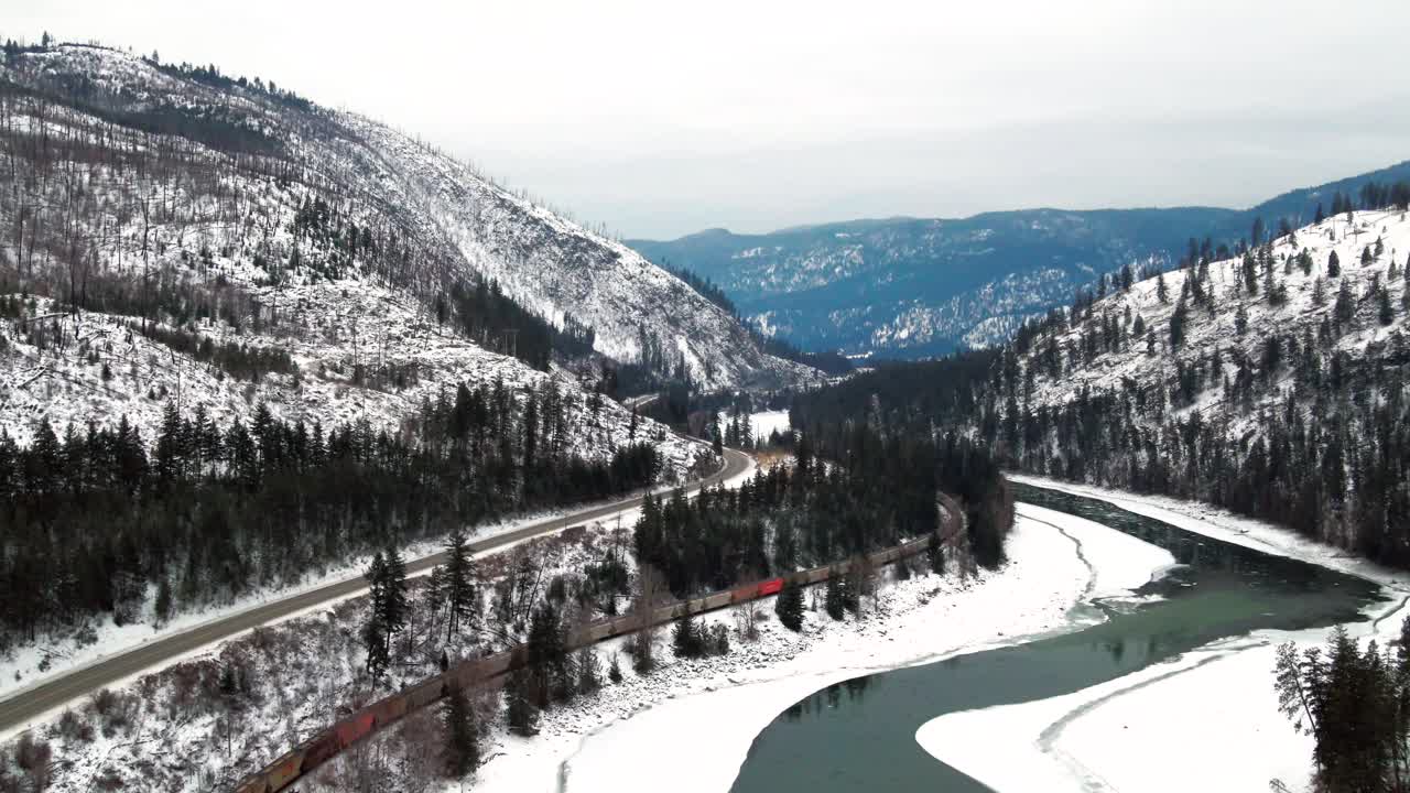 valle congelado del río thompson del norte cerca de kamloops: vista panorámica del paisaje montañoso cubierto de nieve con automóviles en la autopista 5 de cabeza amarilla y tren de carga en el ferrocarril en una amplia toma aérea en bc
