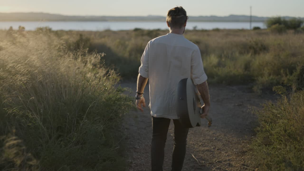Uomo che cammina con la chitarra nella natura al tramonto