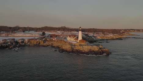 Waves-crashing-below-Portland-Head-Light,-winter-sunrise-STATIONARY-AERIAL