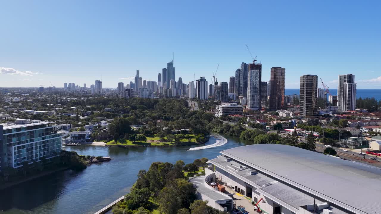 Drone footage captures the scenic Gold Coast skyline and waterfront under clear blue skies, showcasing urban architecture and natural beauty