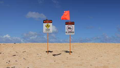 orange flag waving in the wind at no swimming with strong current warning sign at the beach in hawaii