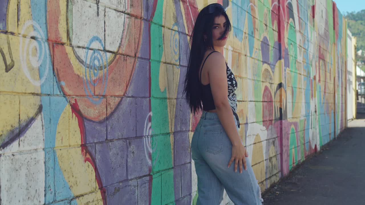 una chica en ropa de calle de moda posa en la ciudad, con graffiti en la pared detrás de ella