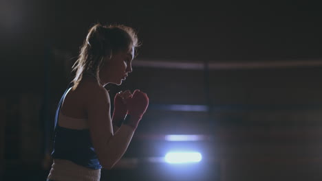 a beautiful woman conducts a shadow fight practicing technique and speed of strikes while training hard for future victories. dark gym background. steadicam shot