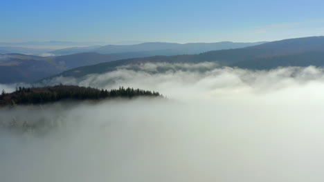 Aerial-rise-above-clouds-to-wide-angle-view-of-mountain-landscape-in-distance