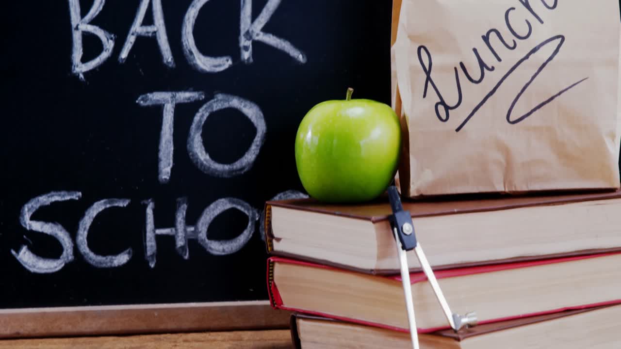 Apfel und Buch mit Schulmaterialien auf dem Tisch.