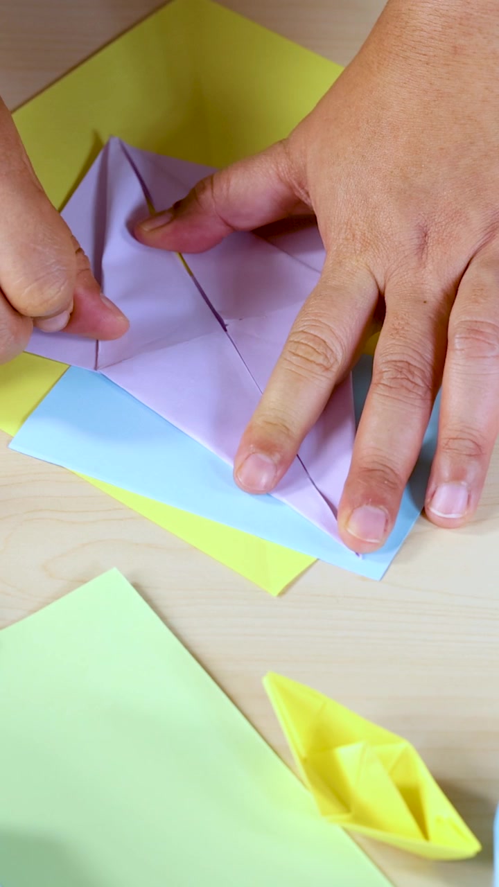 Mani adulte piegano carta pastello in una barca di origami su un tavolo luminoso e ben illuminato.