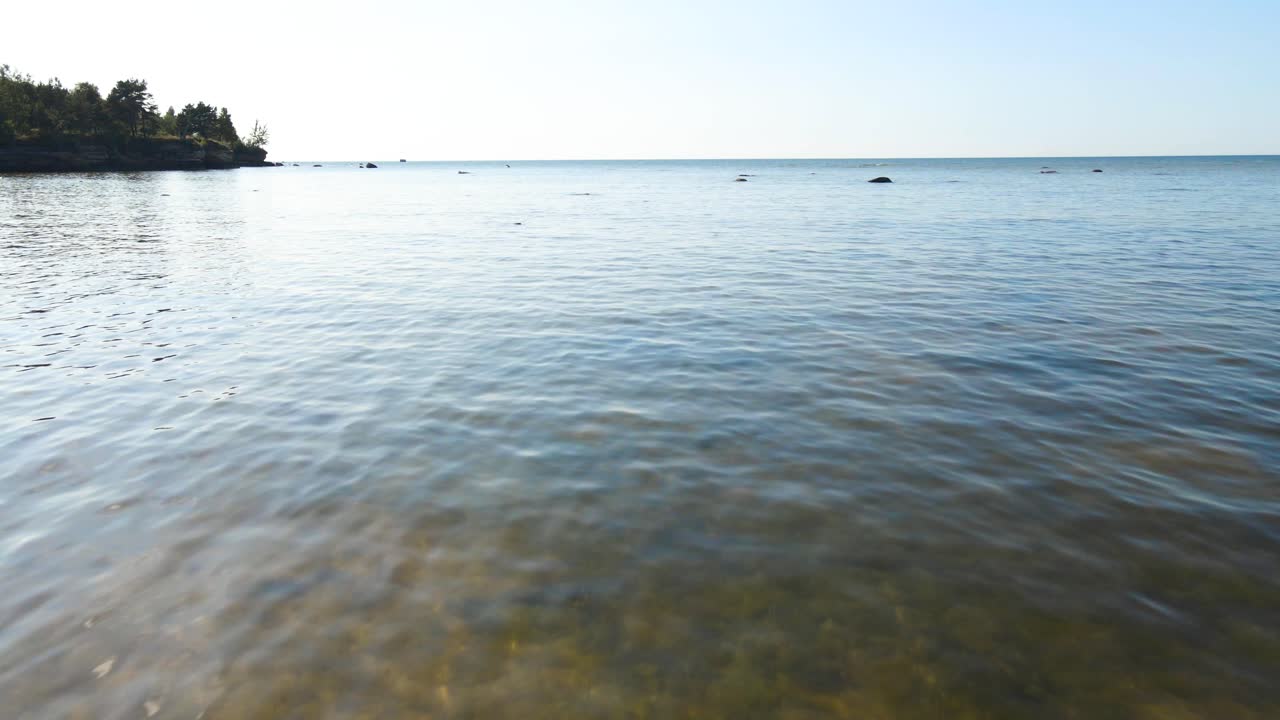 Aerial drone video gliding over a rocky summer time ocean beach shoreline over rocks and shallow ocean blue and green sea water that has small waves and water ripples