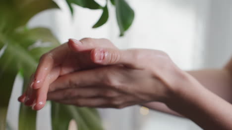 light skin woman with shiny oily hands gently rubbing palms together beside green leaf, in soft natural lighting, emphasizing personal care, relaxation, and wellness in calm indoor atmosphere