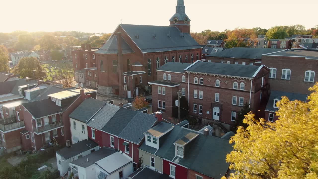 Aerial dolly shot of church cathedral near tight rowhomes in urban Lancaster City, Pennsylvania, cemetery graveyard visible, rising past steeple and rooftops