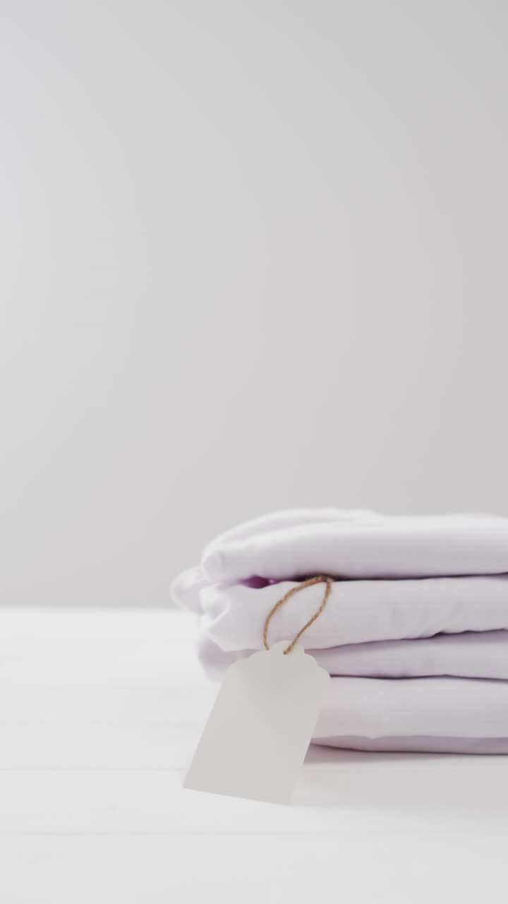 Video verticale di pila di t-shirt bianche piegate con spazio per il testo su sfondo bianco