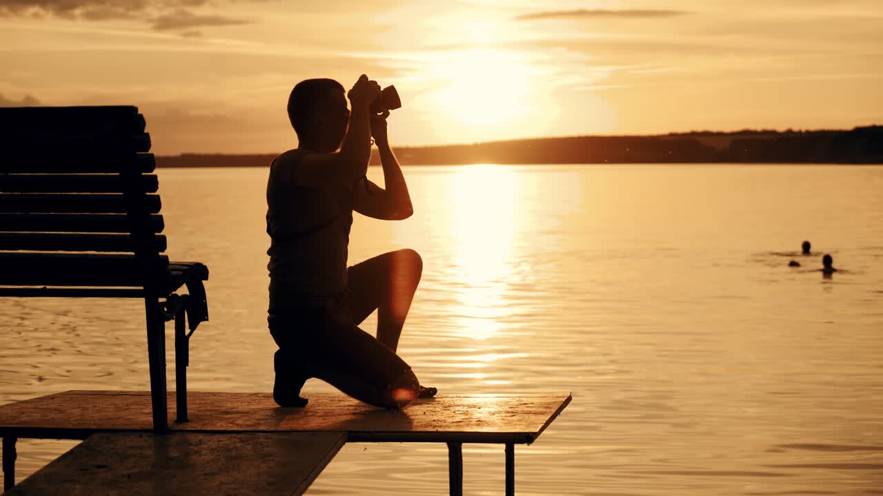 A young photographer was squatting and photographing the sunset on the bridge of the river near bench after which he left that place.