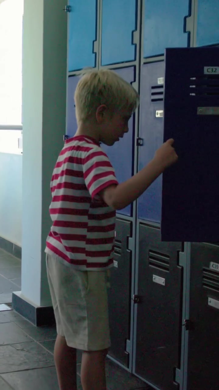 Vertical video: Running boy in red shirt getting bag from locker in hall, placing it by wheelchair