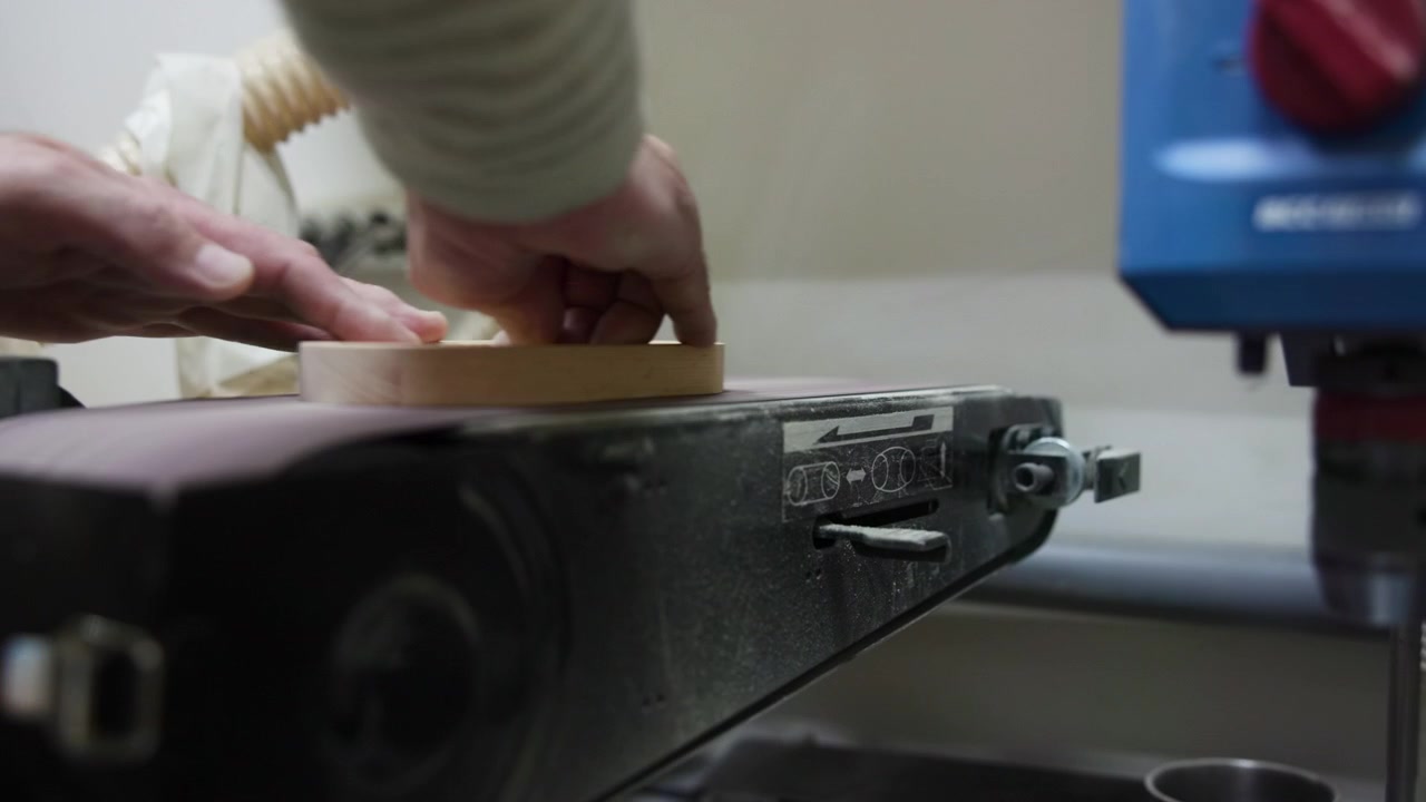 Closeup Hands Sanding Wooden Disc On Belt Sander, Careful Pressure And Steady Motion As Maker Smooths Grain . Media