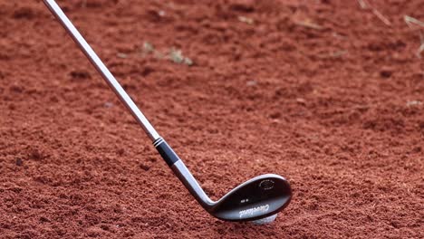 golf club hitting ball, creating a sand trail.
