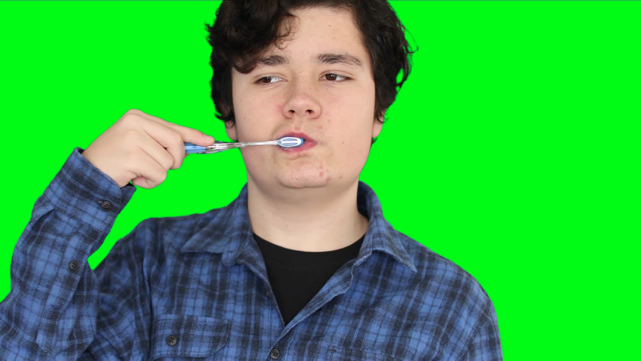 Teenage boy brushing his teeth at green screen background 1