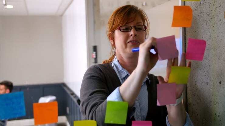 Female executive working on sticky note on glass wall 4k