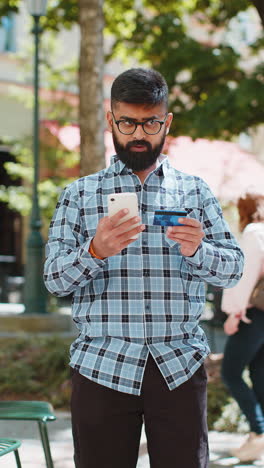 Indian-man-using-credit-bank-card-smartphone-while-transferring-money,-purchases-online-shopping