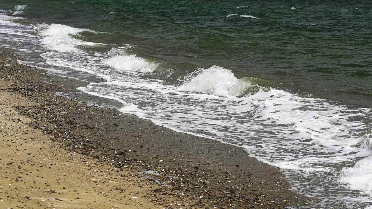 Onde marine calme che lambiscono dolcemente una spiaggia sabbiosa e ciottolosa. Scena costiera serena che mostra la marea che sale con schiuma bianca