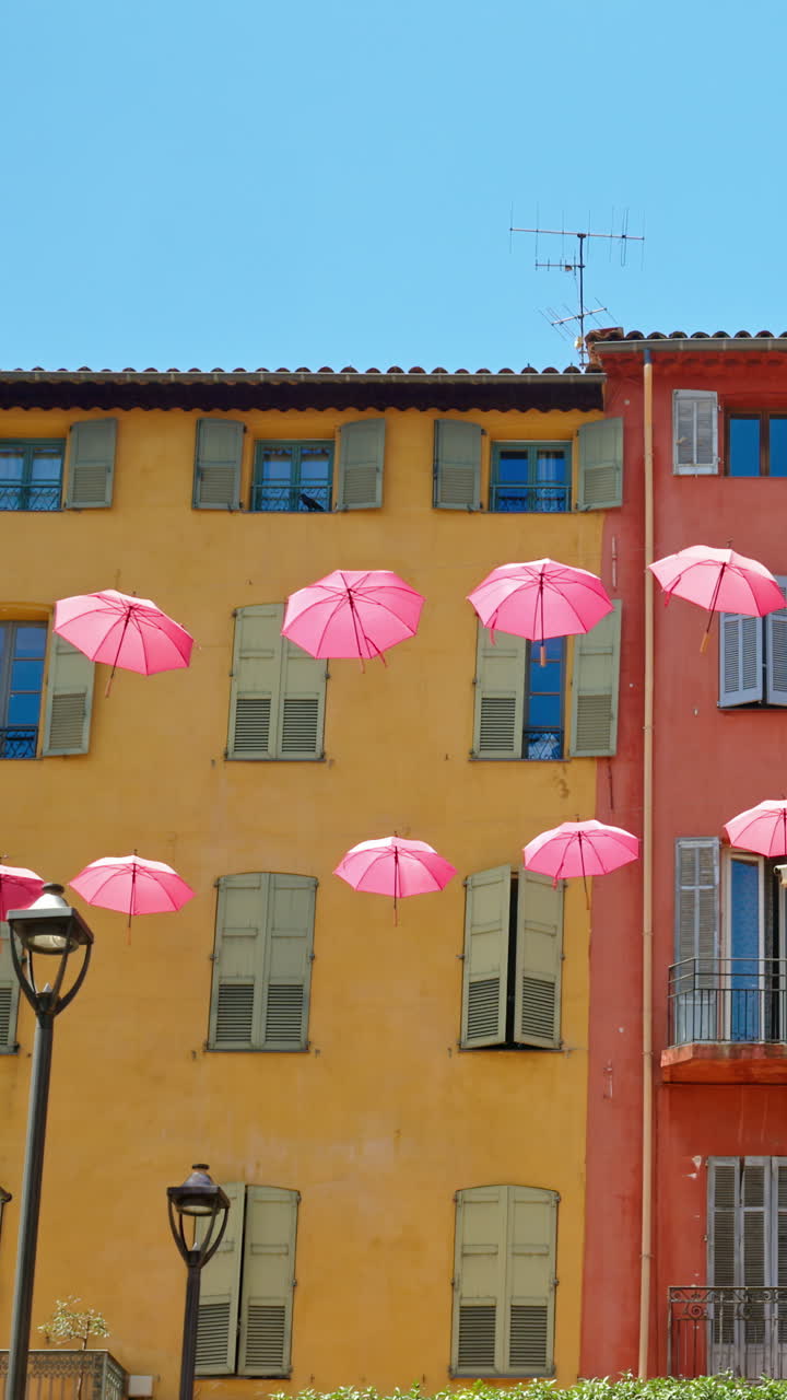 Rows of pink umbrellas above the streets of the old town in Grasse, France. Vertical