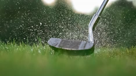 golf club hits a golf ball in a super slow motion. drops of morning dew and grass particles rise into the air after the impact.