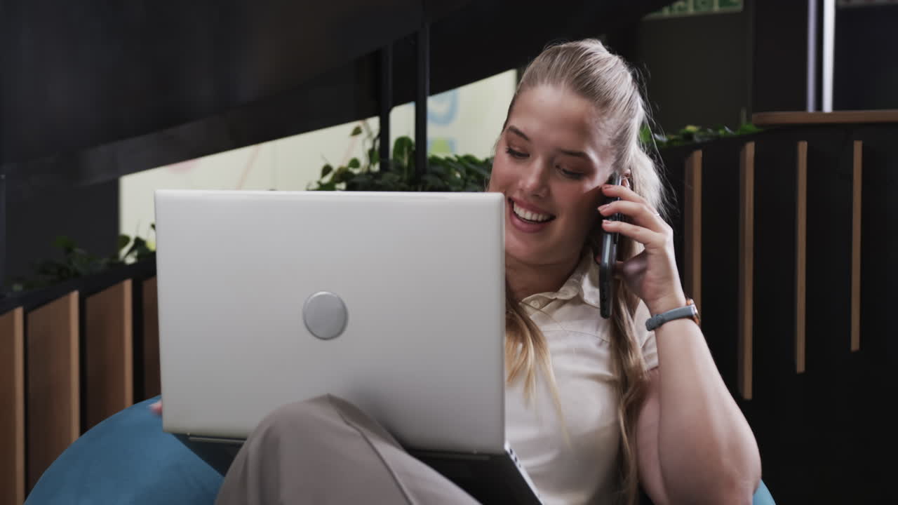 Using laptop and talking on smartphone, woman working from home office