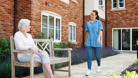 senior woman sitting on bench and talking with nurse in retirement home