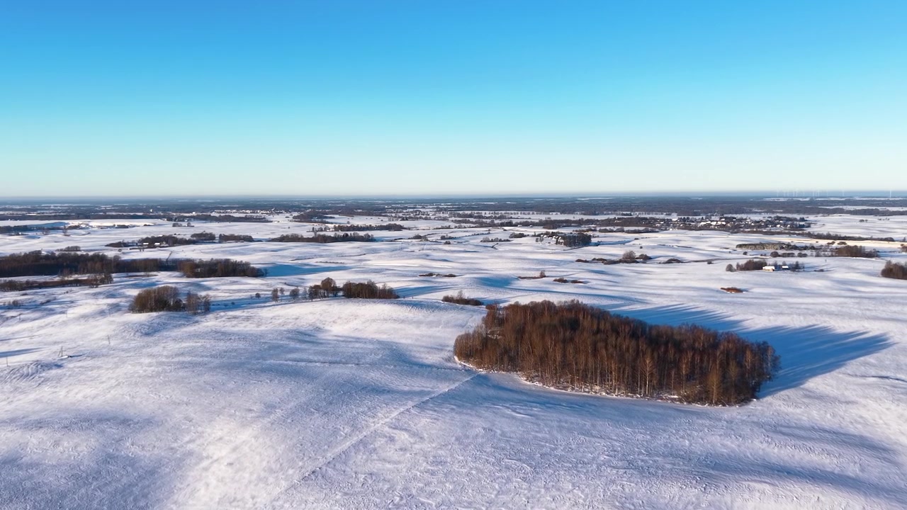 Fantastisk dronevideo glir over et vidstrakt snødekt landskap på landsbygda og et isolert skogområde. Klar vinterbelysning, klar blå himmel og en rolig panoramisk komposisjon skaper en fredfull skjønnhet