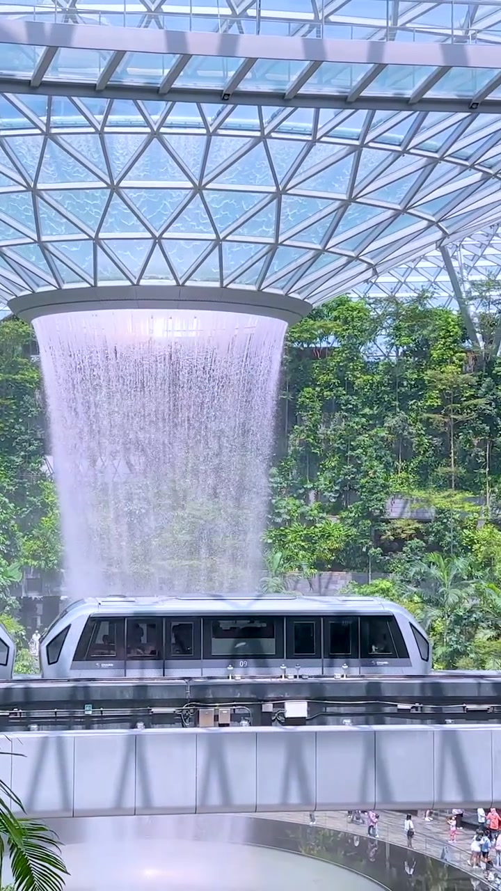 Un moderno treno automatizzato scivola oltre un'enorme cascata interna e una rigogliosa vegetazione tropicale.
