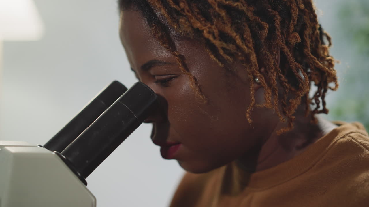mujer afroamericana examina bacterias a través del microscopio
