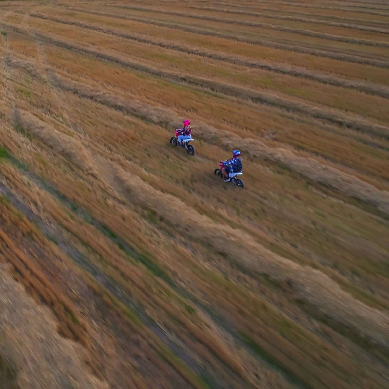 Guy in blue helmet follows girl in pink helmet in motorbike ride. Young couple enjoying summer riding in the farmlands. Top view