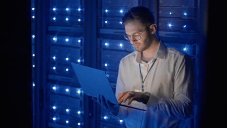 Ingeniero-De-Servidores-Masculino-En-El-Centro-De-Datos.-Ingeniero-De-TI-Inspeccionando-Un-Gabinete-De-Servidor-Seguro-Utilizando-Tecnología-Moderna-De-Coworking-De-Computadoras-Portátiles-En-El-Centro-De-Datos.