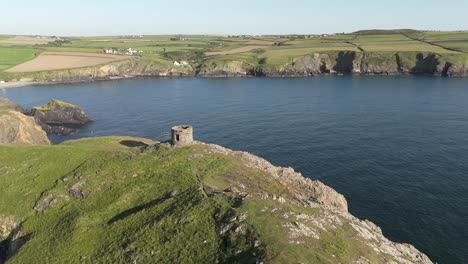 An-aerial-view-of-Abereiddi-Tower-in-Pembrokeshire,-South-Wales,-on-a-sunny-evening-with-a-clear-blue-sky