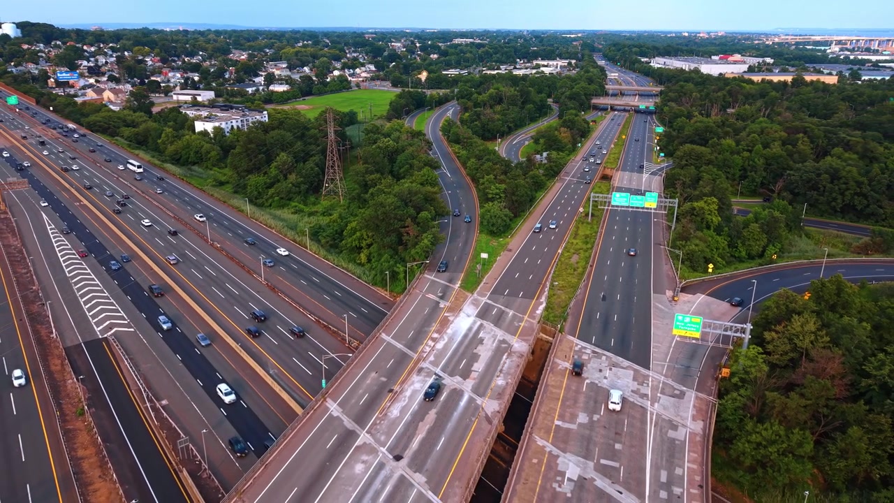 Elevated perspective of highway lane split and signs, New Jersey. View showing concrete road deck, moving vehicles and lush green trees.