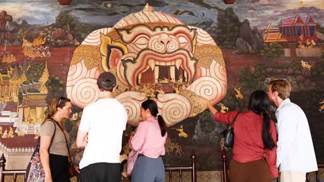 group examines intricate mural in bangkok temple