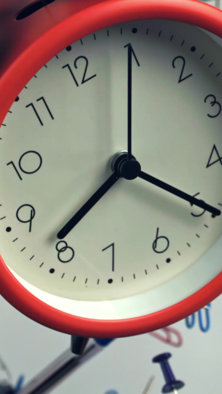 Red Alarm Clock Ticking Amidst Blurred Office Supplies