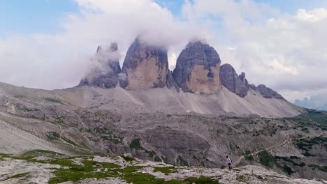 drone pans right following solo traveler trekking towards the dolomites