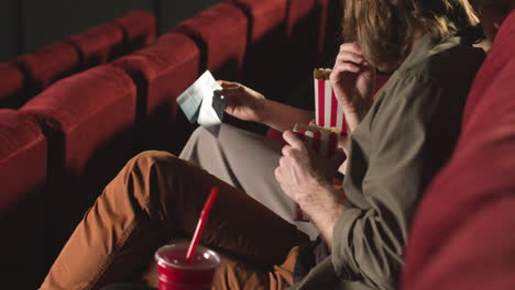 rear view of couple sitting on cineam seats looking at the cinema tickets and holding popcorn and drinks