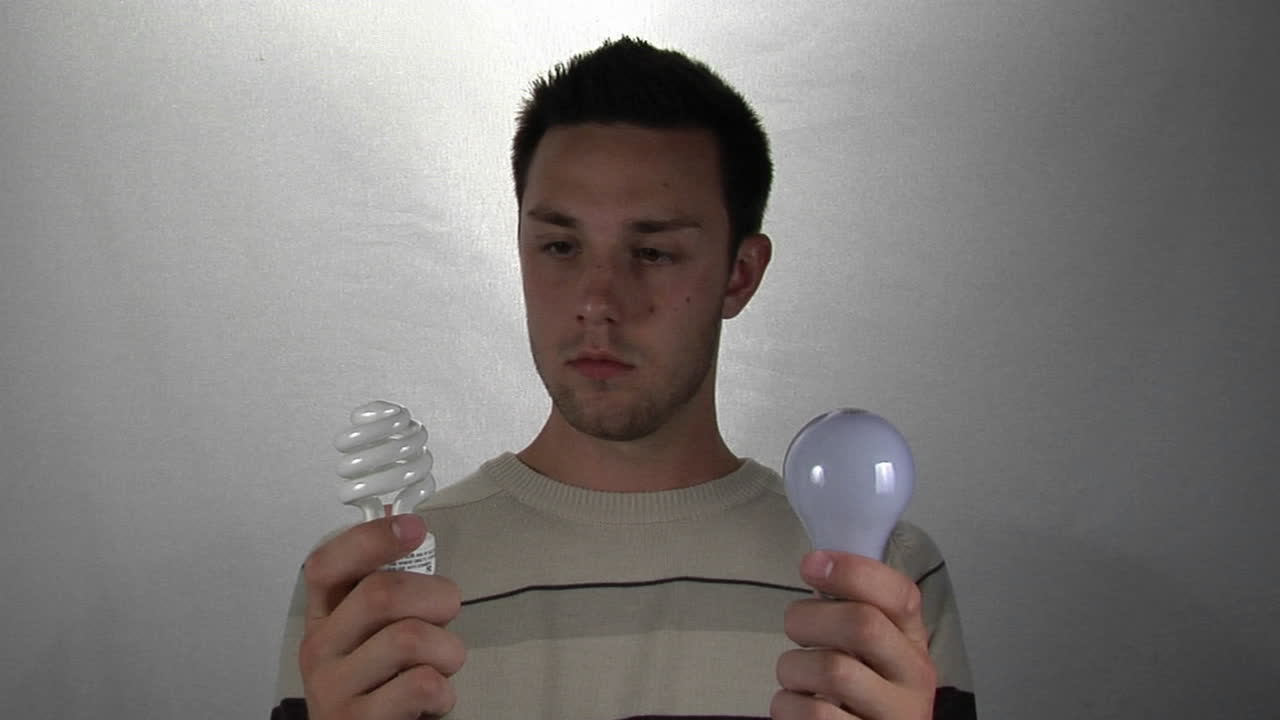 한 남자가 한 손에는 소형 형광 전구를, 다른 한 손에는 표준 전구를 들고 있습니다.