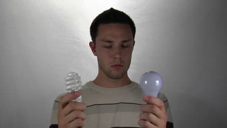 a man holds a compact-fluorescent light bulb in one hand and a standard light bulb in the other