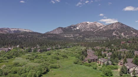 4k drone footage camera tilt up of beautiful mammoth mountain in the summertime with a view of a lush green meadow and cabins