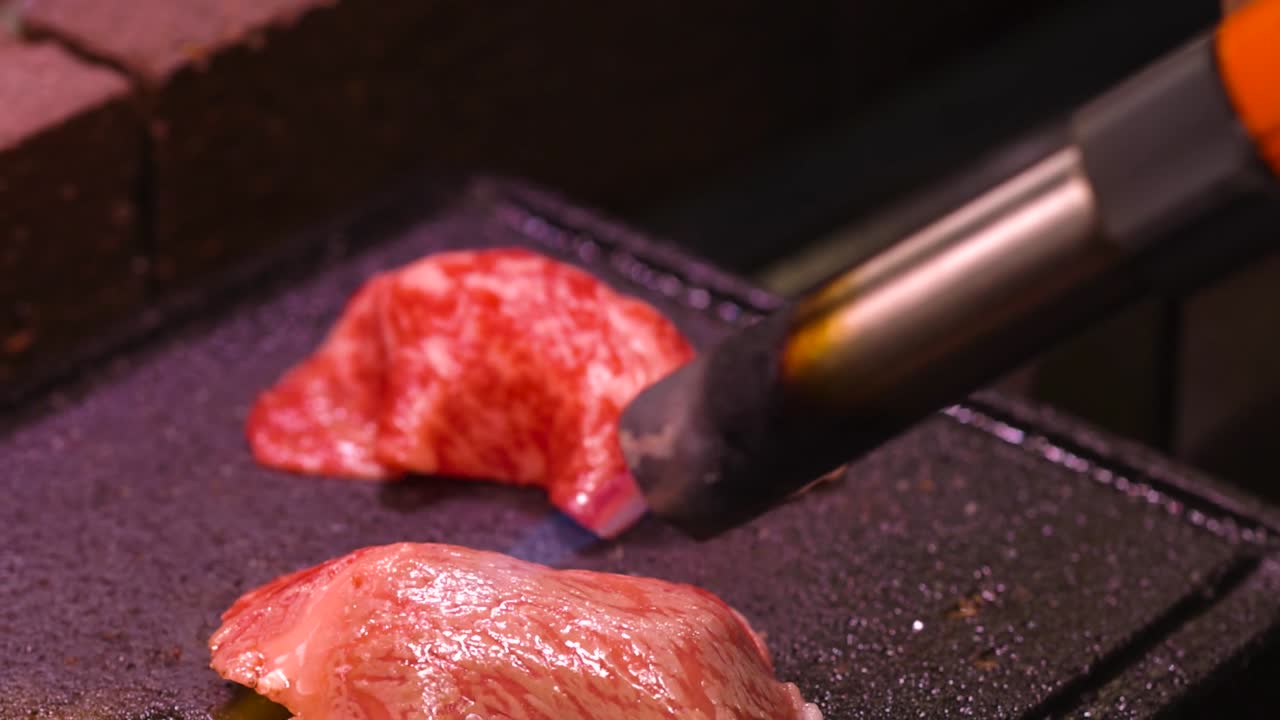 Un cannello da cucina brucia sottili fette di manzo marmorizzato su una piastra in pietra.