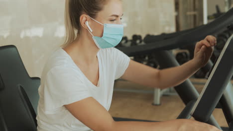 young athlete female with face mask uses a smartphone and an exercise machine in the gym. close-up.