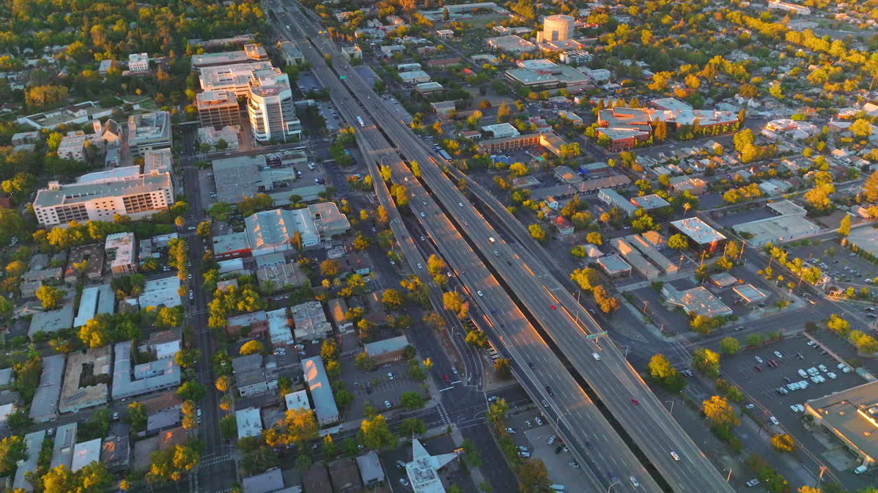 Multilane two-ways roads along the big city. Green city panorama in the rays of setting sun. Aerial view.
