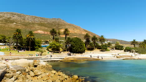 Panning-shot-back-toward-Seaforth-beach-with-beachgoers,-Simon's-Town