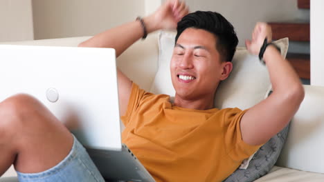 relaxing at home, asian man smiling with laptop on couch, enjoying leisure time