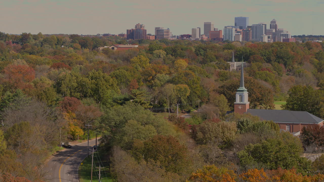 지평선에 도시 스카이라인이 있는 가을 나무 사이의 도로와 교회의 전망